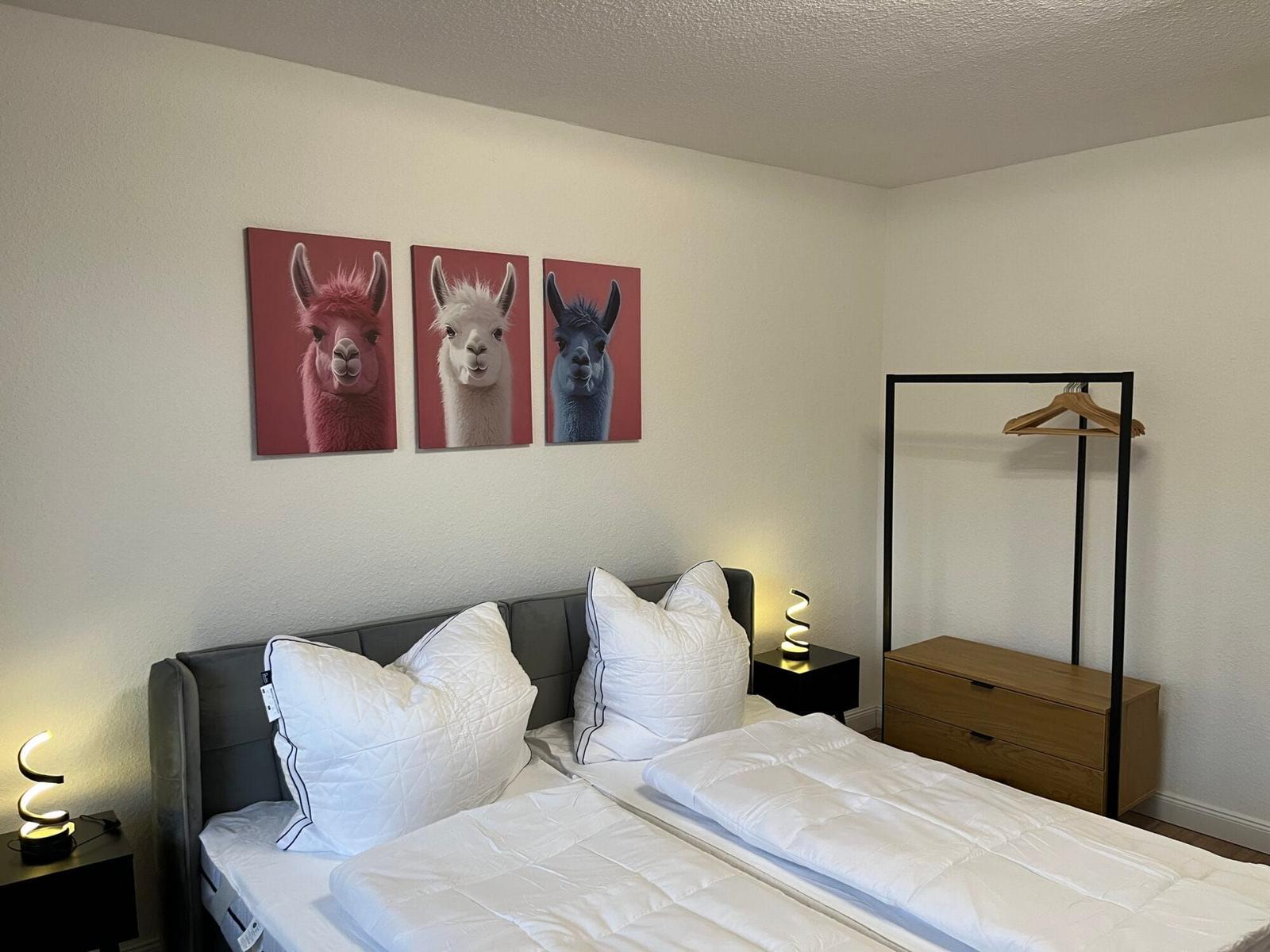Schlafzimmer mit Doppelbett, Wandbildern von Lamas und Kleiderschrank.