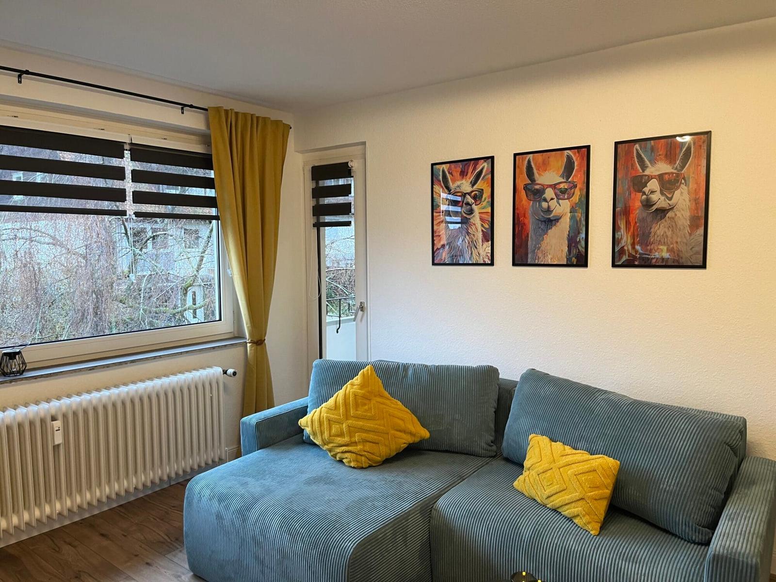 Ein Wohnzimmer mit blauem Sofa, gelben Kissen und drei Wandbildern von Lamas.