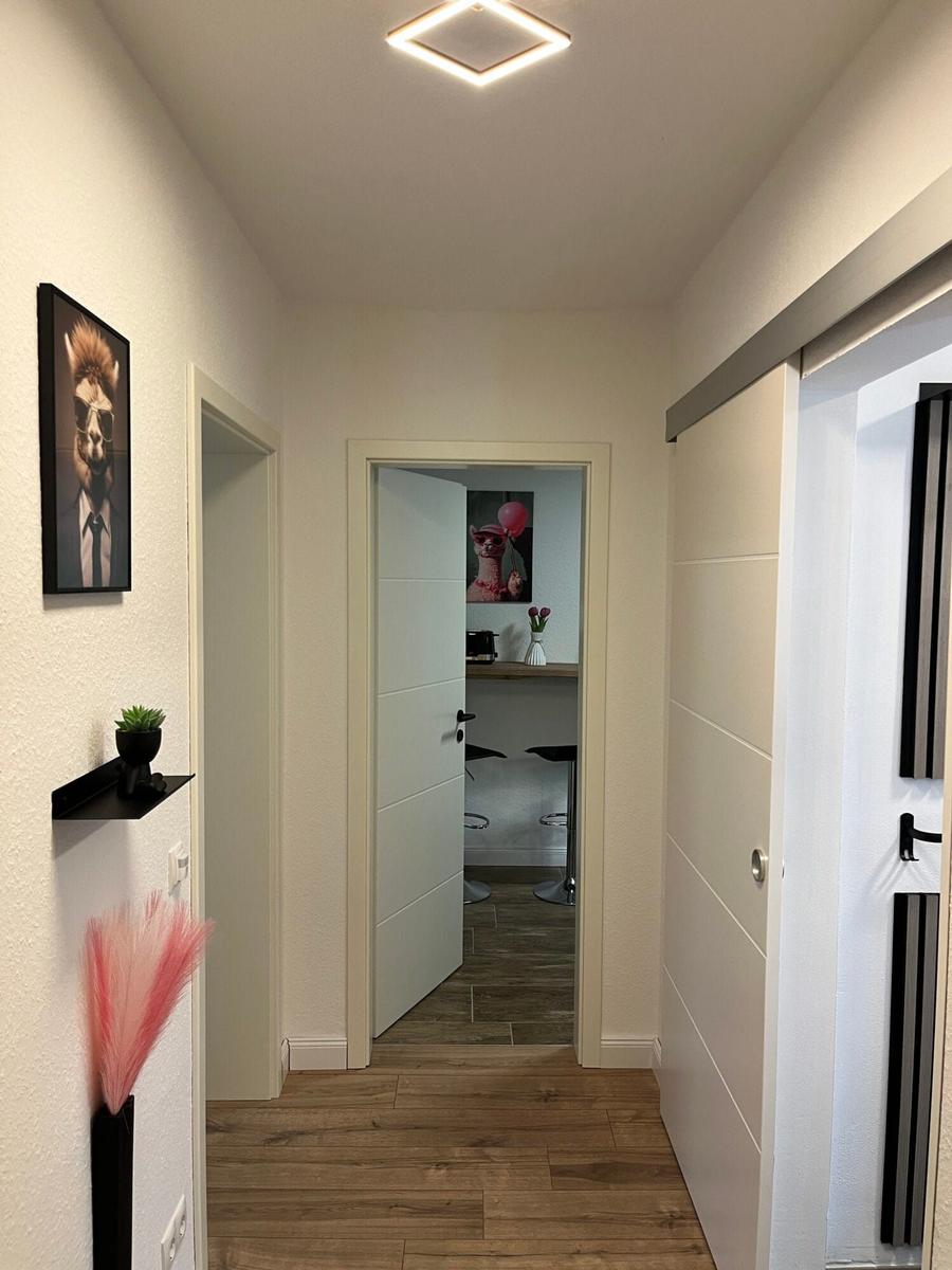 Flur mit Holzboden, Wandbild und Blick in Küche mit Barhocker.