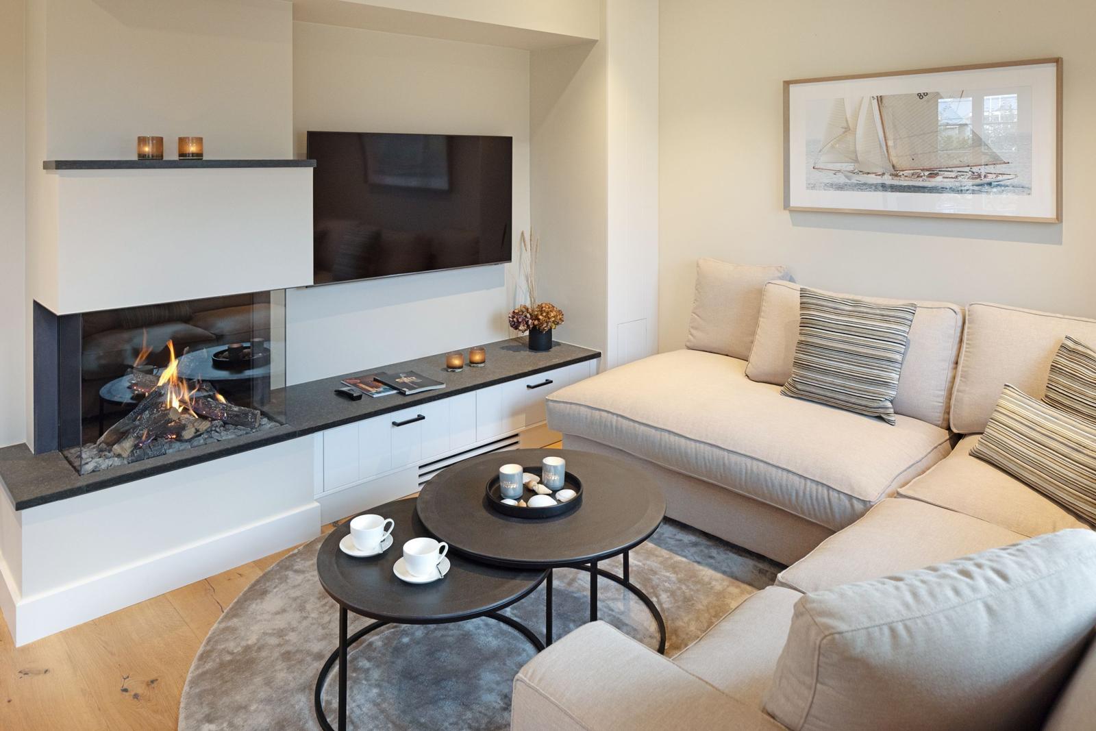 Wohnzimmer mit Sofa, Kamin und Fernseher. Runde Tische und Wandbild mit Segelyacht.