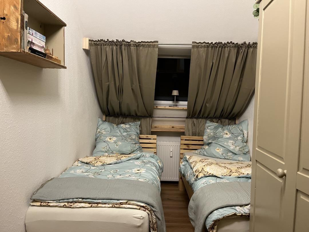 Two single beds with blue bedding are under a window with curtains.