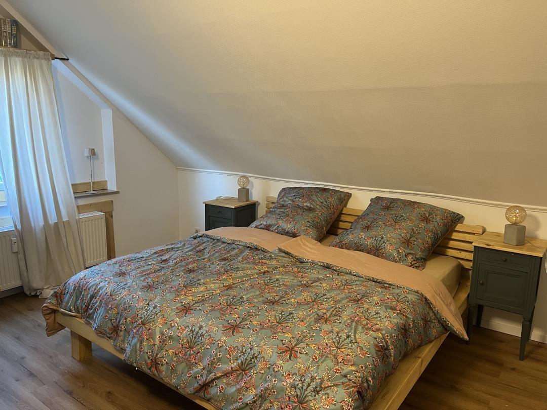 Bedroom with sloped ceiling, wooden floor, and bed with patterned bedding.