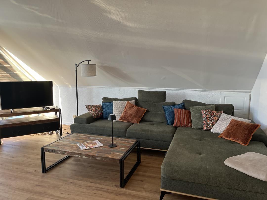 Living room with green sofa, coffee table, and TV under sloped ceilings.