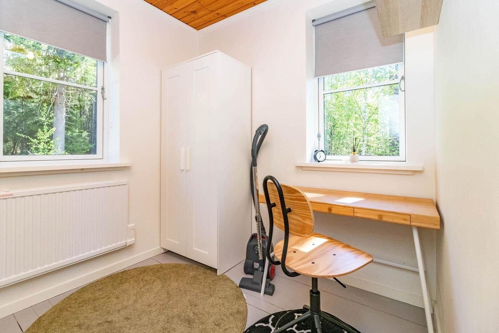 Zimmer mit Schreibtisch, Stuhl, Kleiderschrank und Fenstern mit Waldblick.