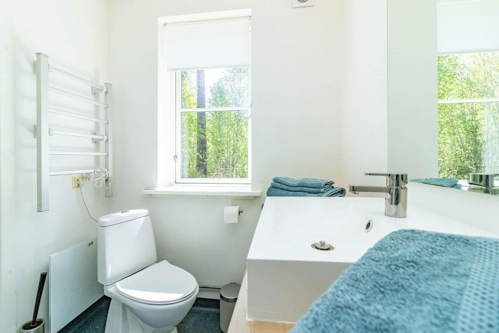 Badezimmer mit Toilette, Waschbecken und Fenster zum Wald.