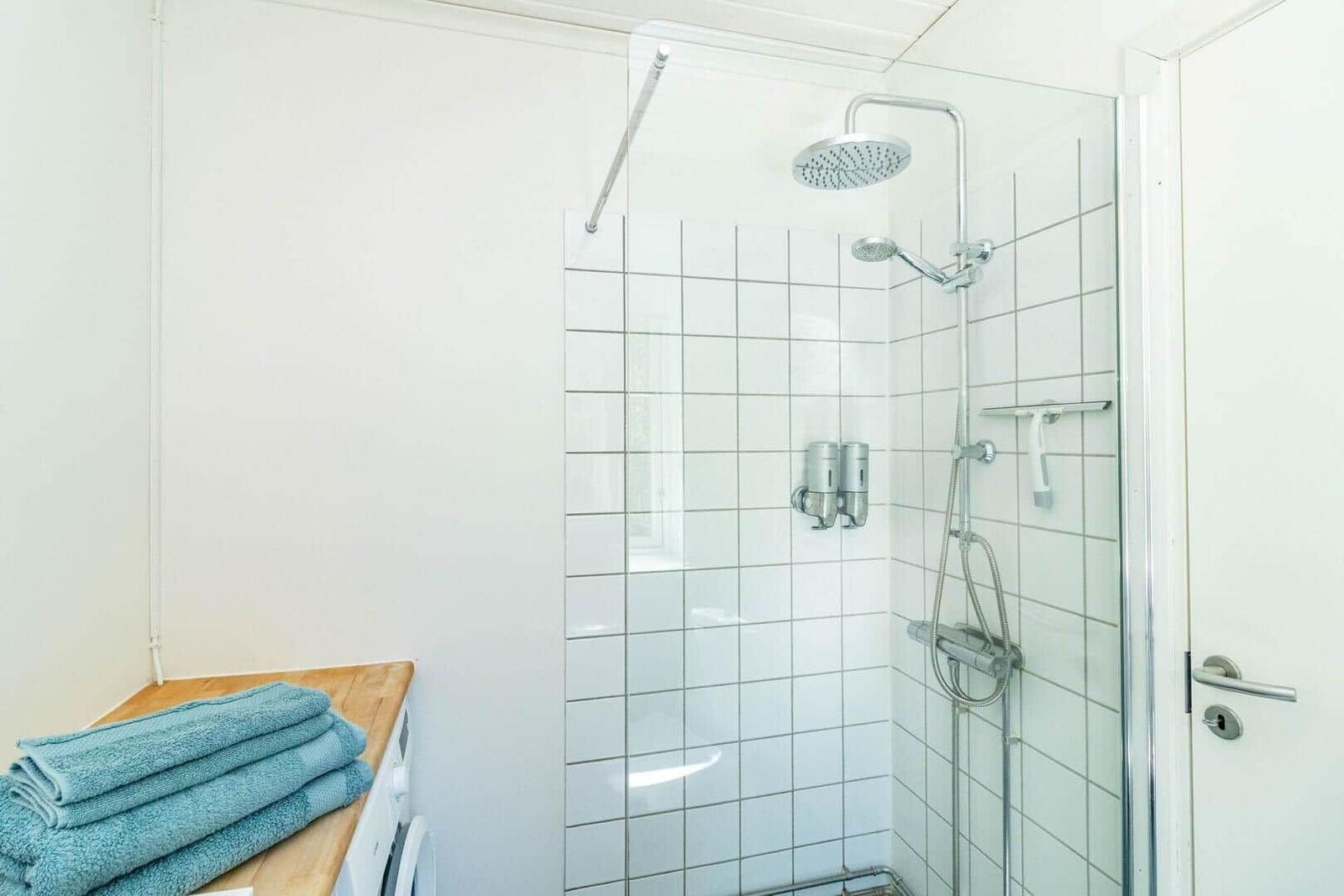 Bad mit Dusche, weißen Fliesen und blauen Handtüchern auf Holzoberfläche.