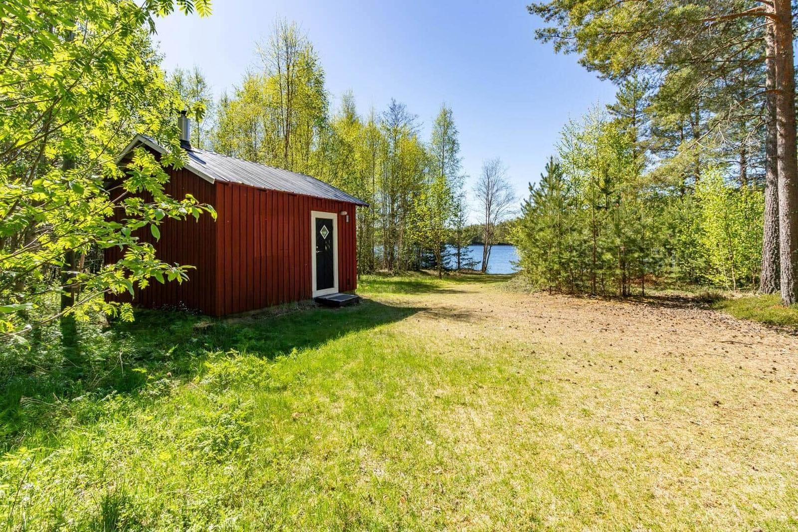Rotes Holzhaus mit weißer Tür, umgeben von Bäumen und einem See.