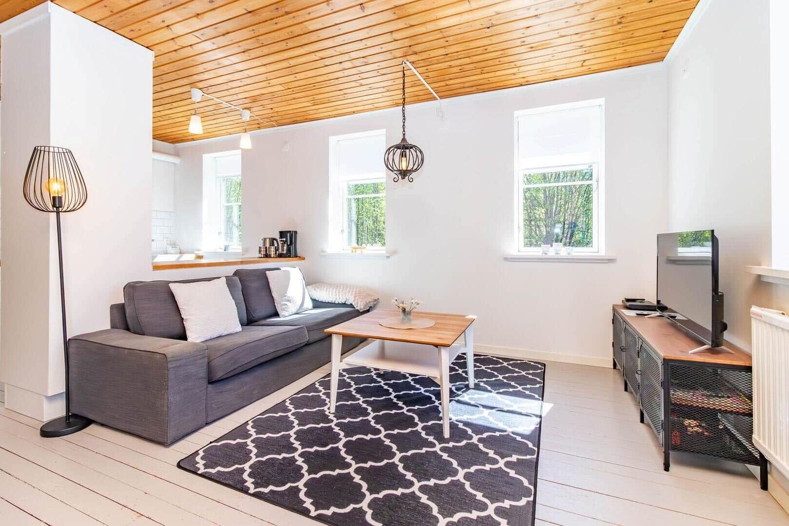 Wohnzimmer mit Sofa, Couchtisch und Fernseher. Holzdecke und Fenster mit Blick auf Grün.