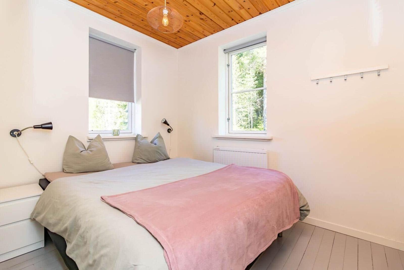 Schlafzimmer mit Bett, Fenstern und Holzdecke.