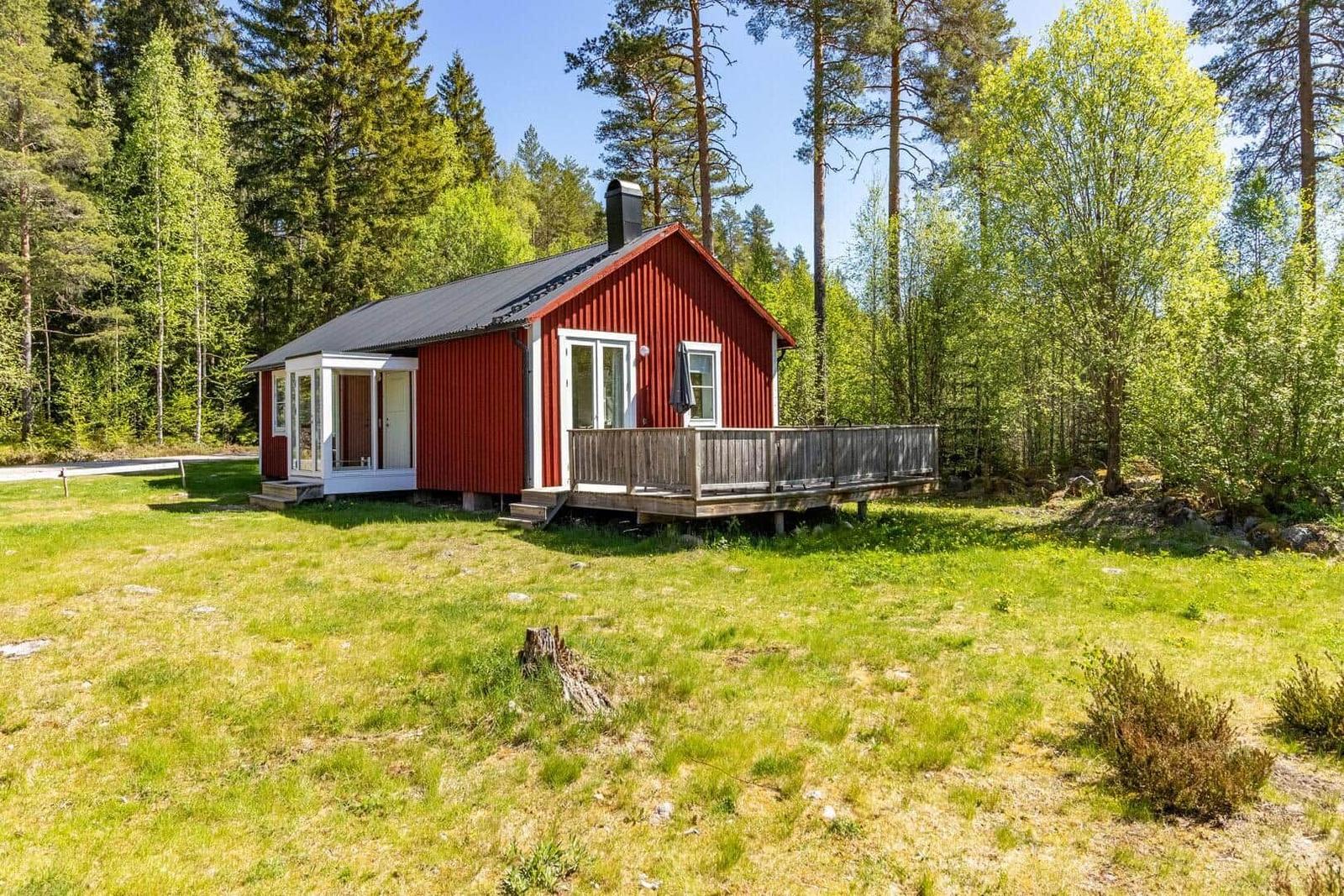 Rotes Holzhaus mit Terrasse im Wald. Grasfläche vor dem Haus.