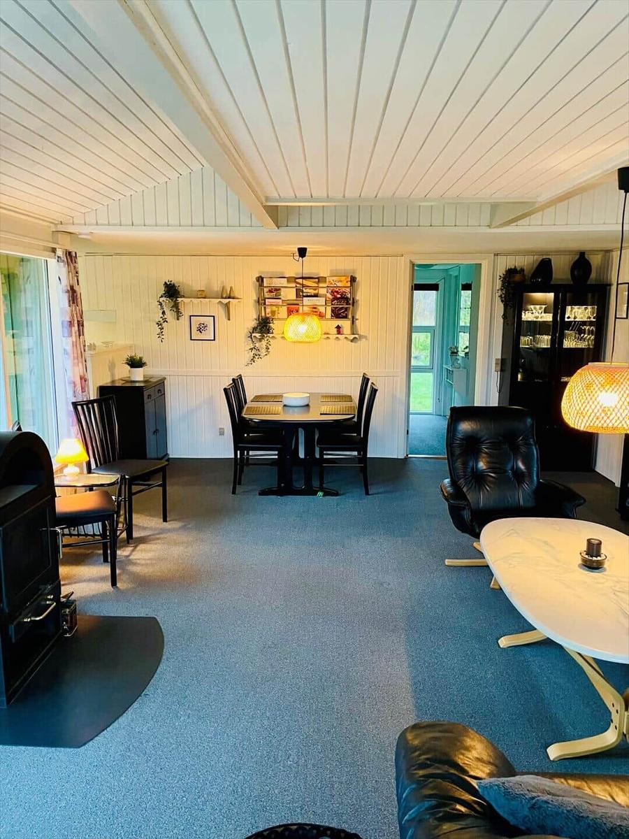Living and dining area with table, chairs, sofa and fireplace. Wooden walls and blue carpet.