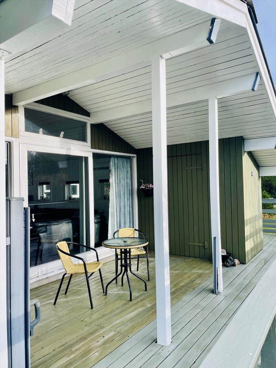Deck with table and two chairs under white roof. Wooden planks and green walls.