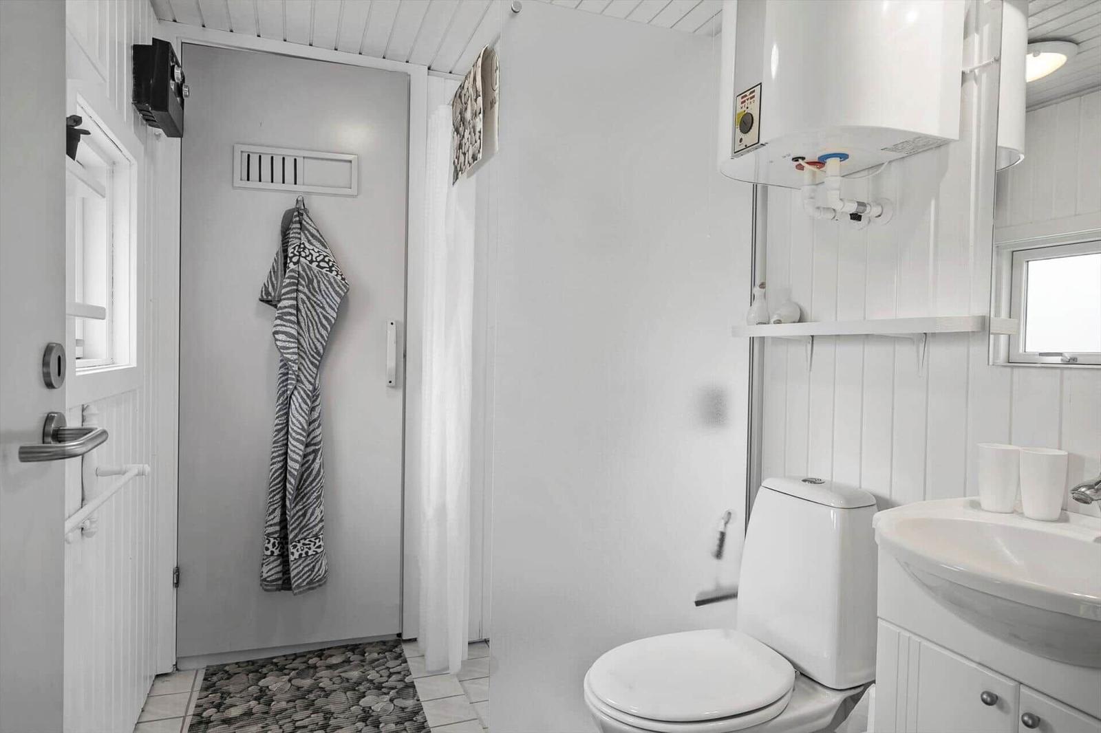 Bathroom with toilet, sink, and shower. White walls and a gray rug.