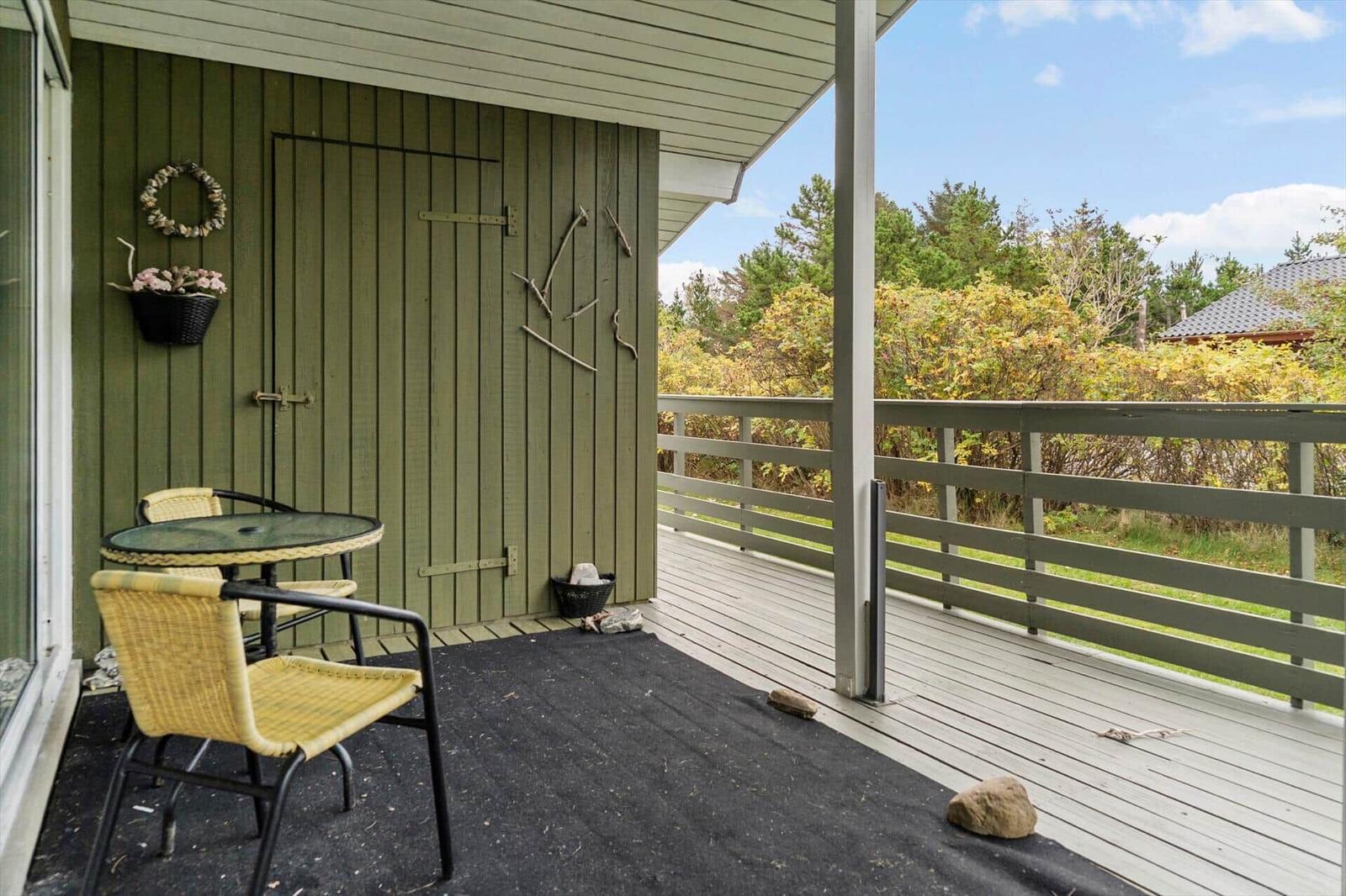 Deck with table and chairs, green wood wall, view of forest.