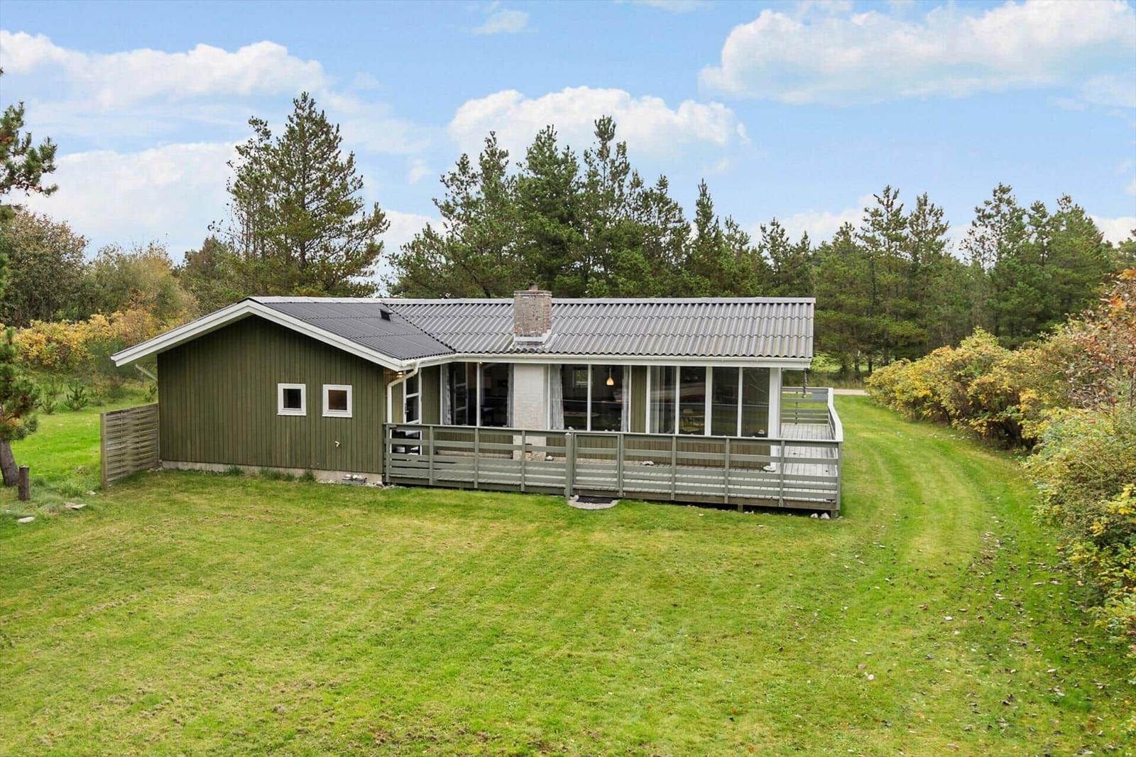 A house with green cladding and large veranda in the grassland.