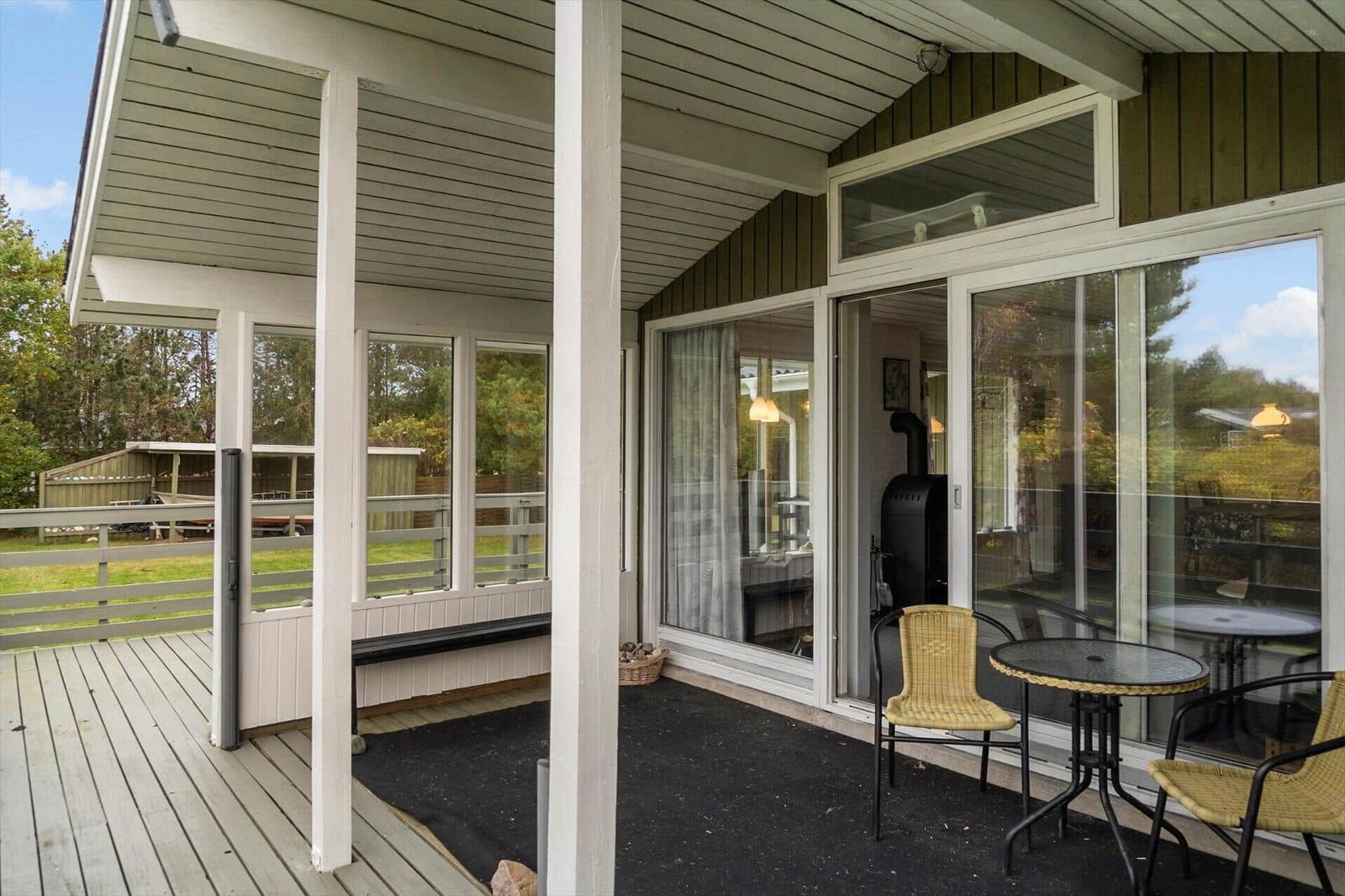 Deck with seating area and glass door to house. Wooden floor and garden in background.