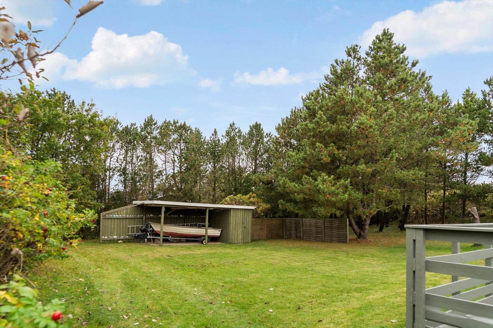 Backyard with boat shed, lawn, and trees under blue sky.
