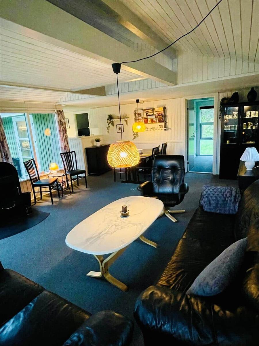 Living room with leather sofa, dining table, and ceiling fan. Light wall paneling and large windows.