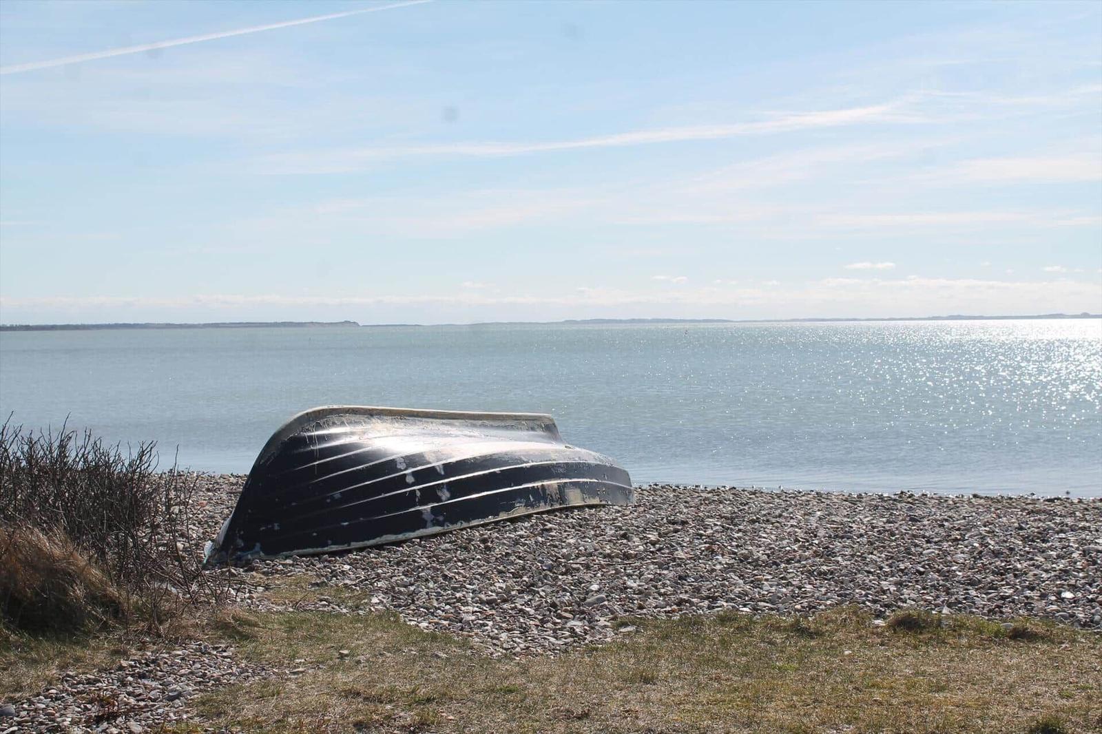 A black boat rests on a pebble beach before calm sea under blue sky.