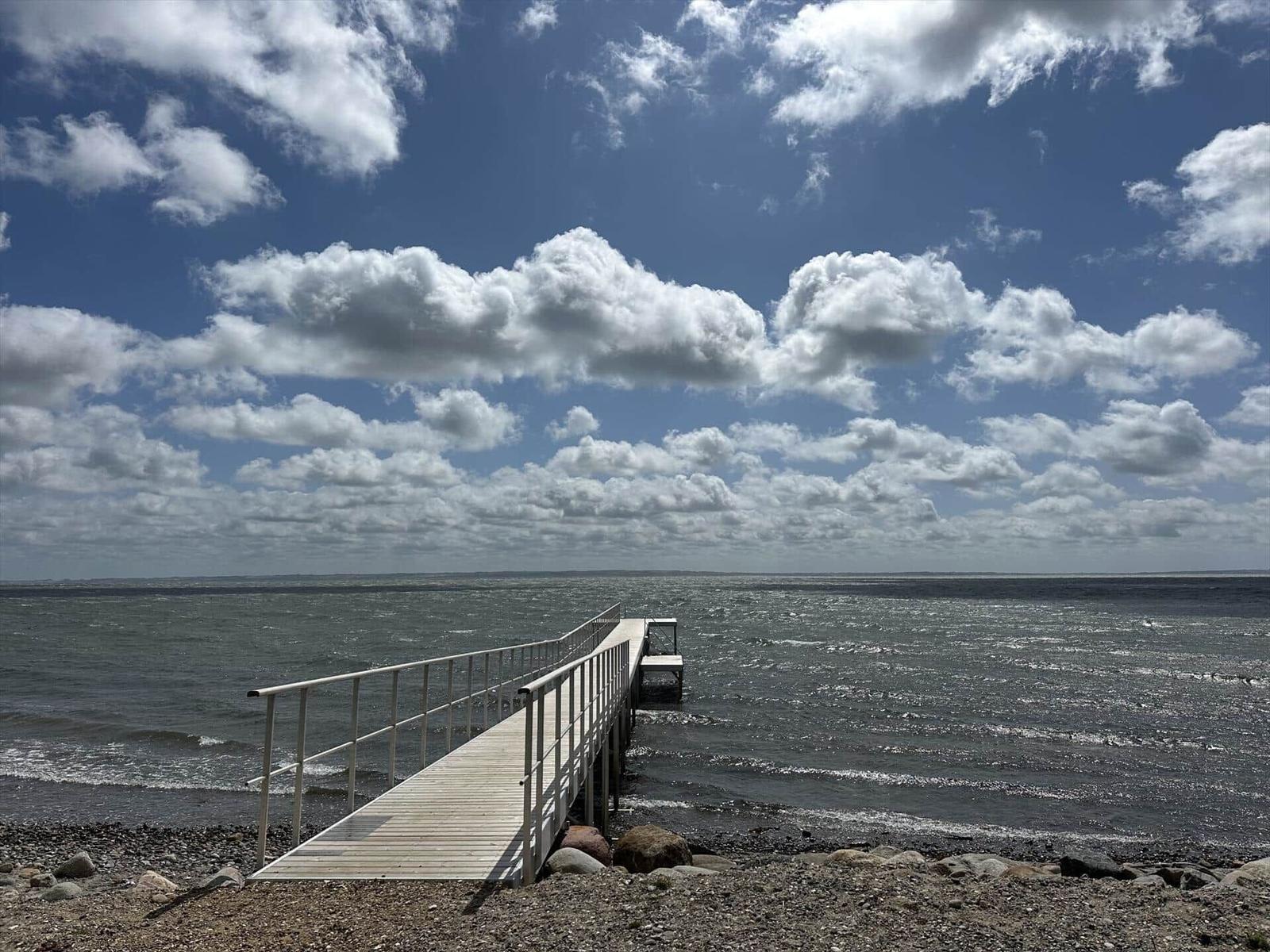 Wooden pier leads to the sea. Blue sky with white clouds.