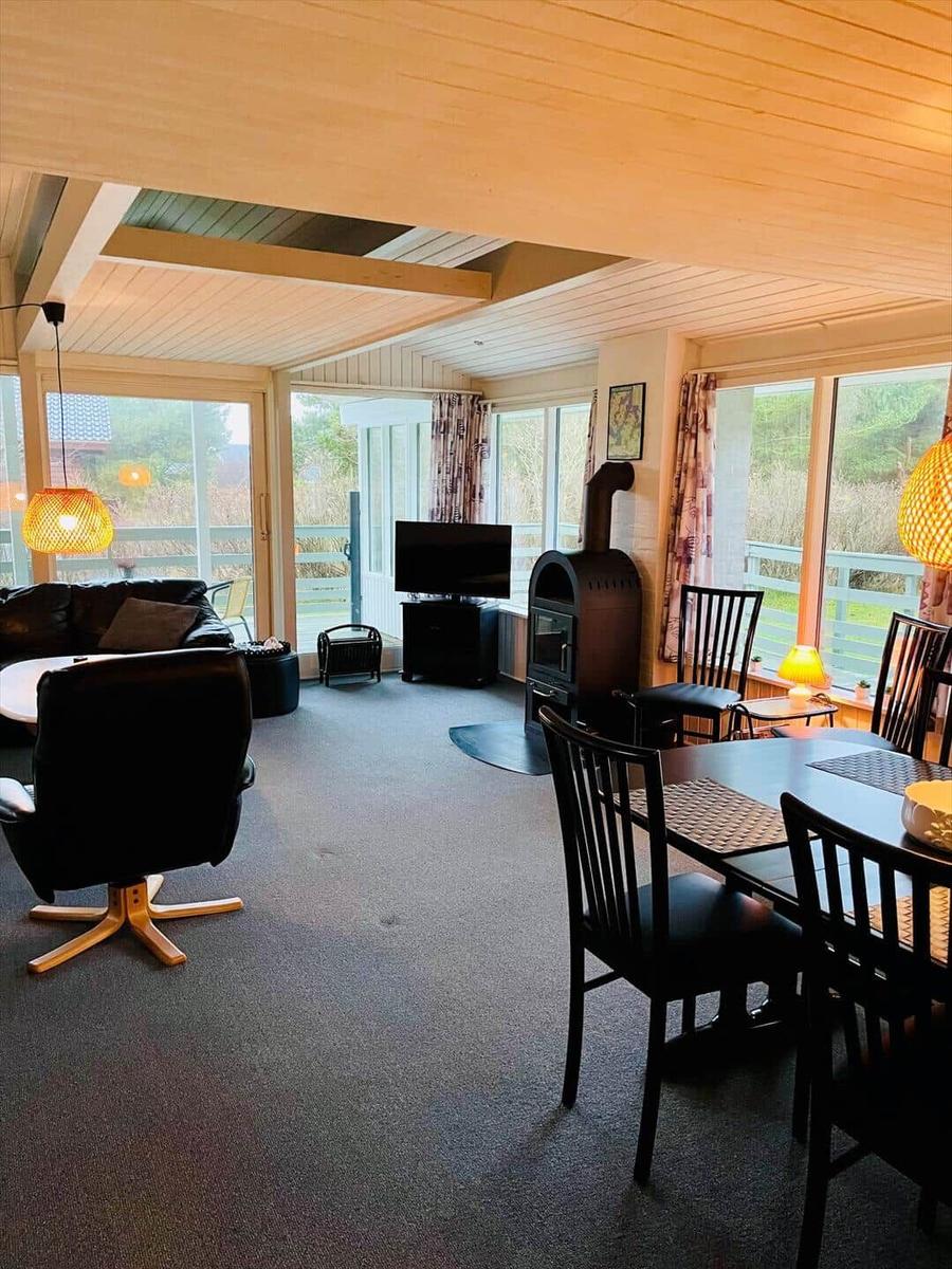 Living and dining area with wooden ceiling, TV, wood stove, and large windows.