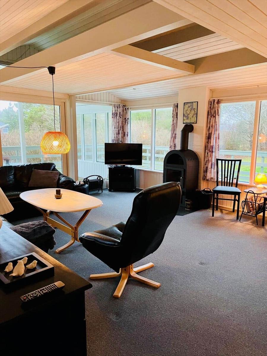 Living room with seating, TV, and wood stove. Large windows offer ample daylight.