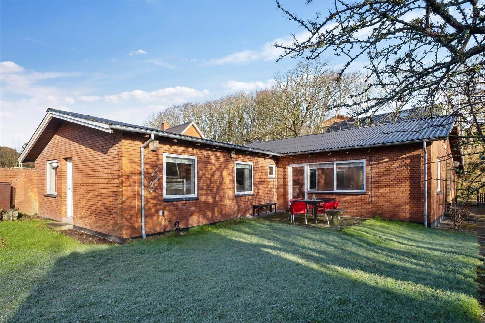 A red brick house with a garden and terrace with red chairs.