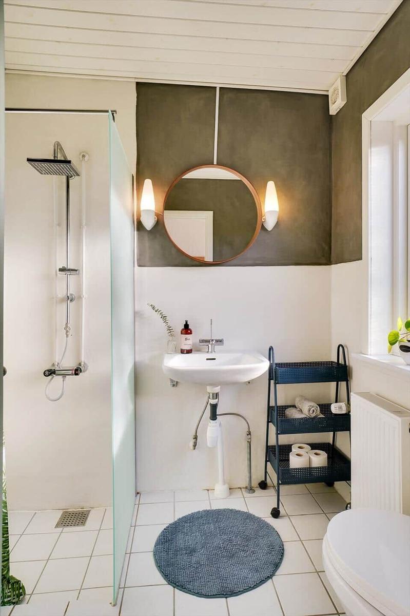 Bathroom with shower, sink, and toilet. Round mirror and blue rug.