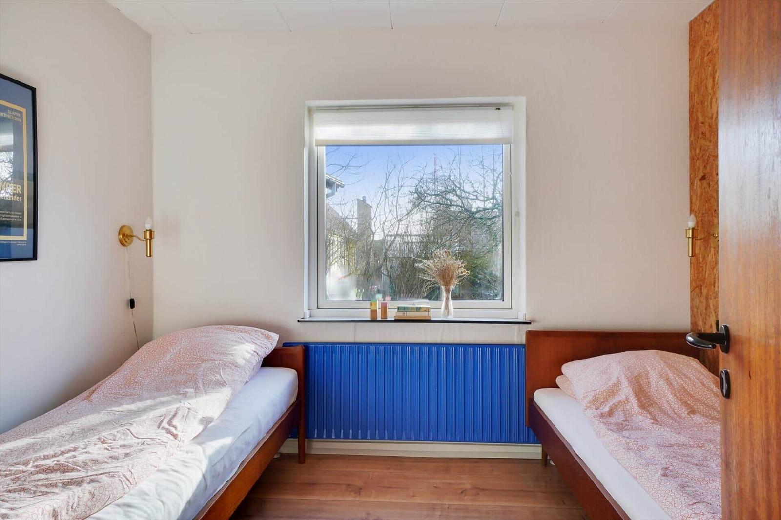 Two beds with pink bedding stand by a window with a blue radiator below.