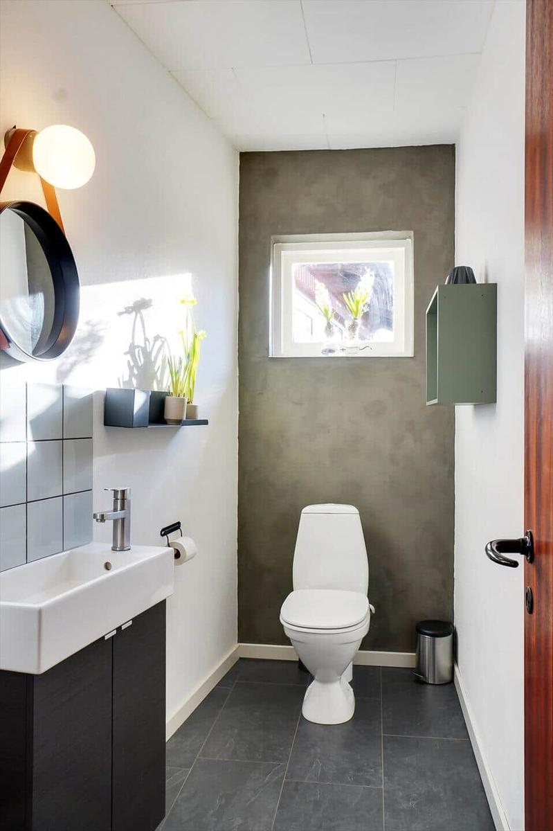 Bathroom with toilet, sink, and window. Gray wall, dark tiles.