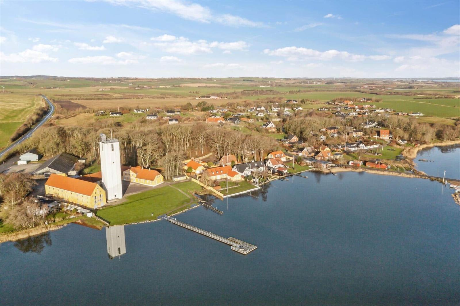 Aerial view of a village by water with houses, a church tower, and surrounding fields.
