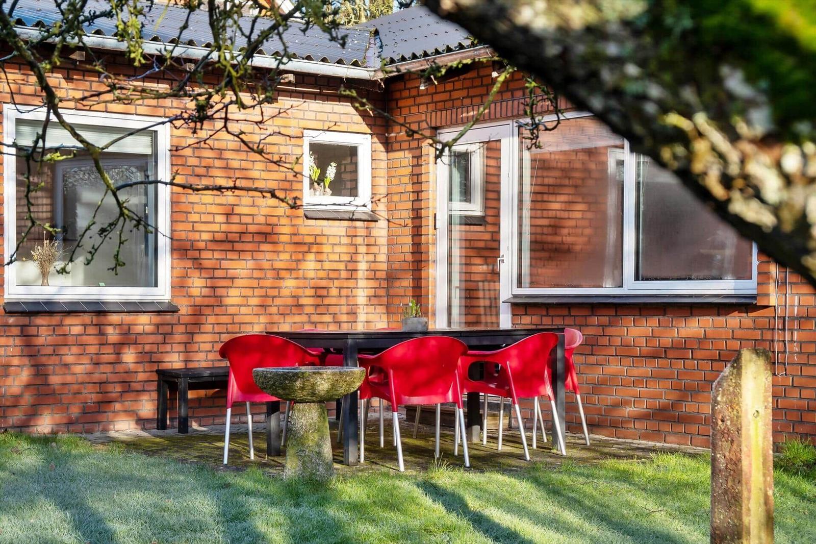 Red seating area with table and stone basin in garden in front of brick house.