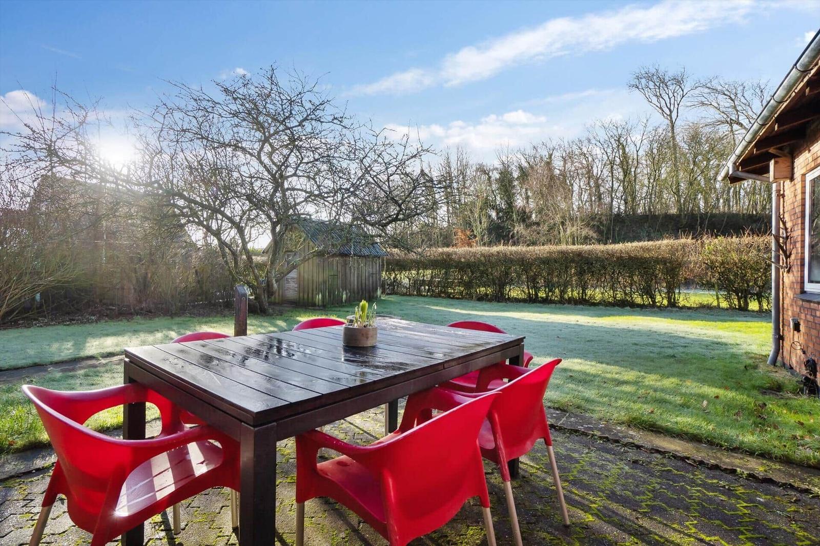 Backyard with table and red chairs, lawn and hedge in the background.