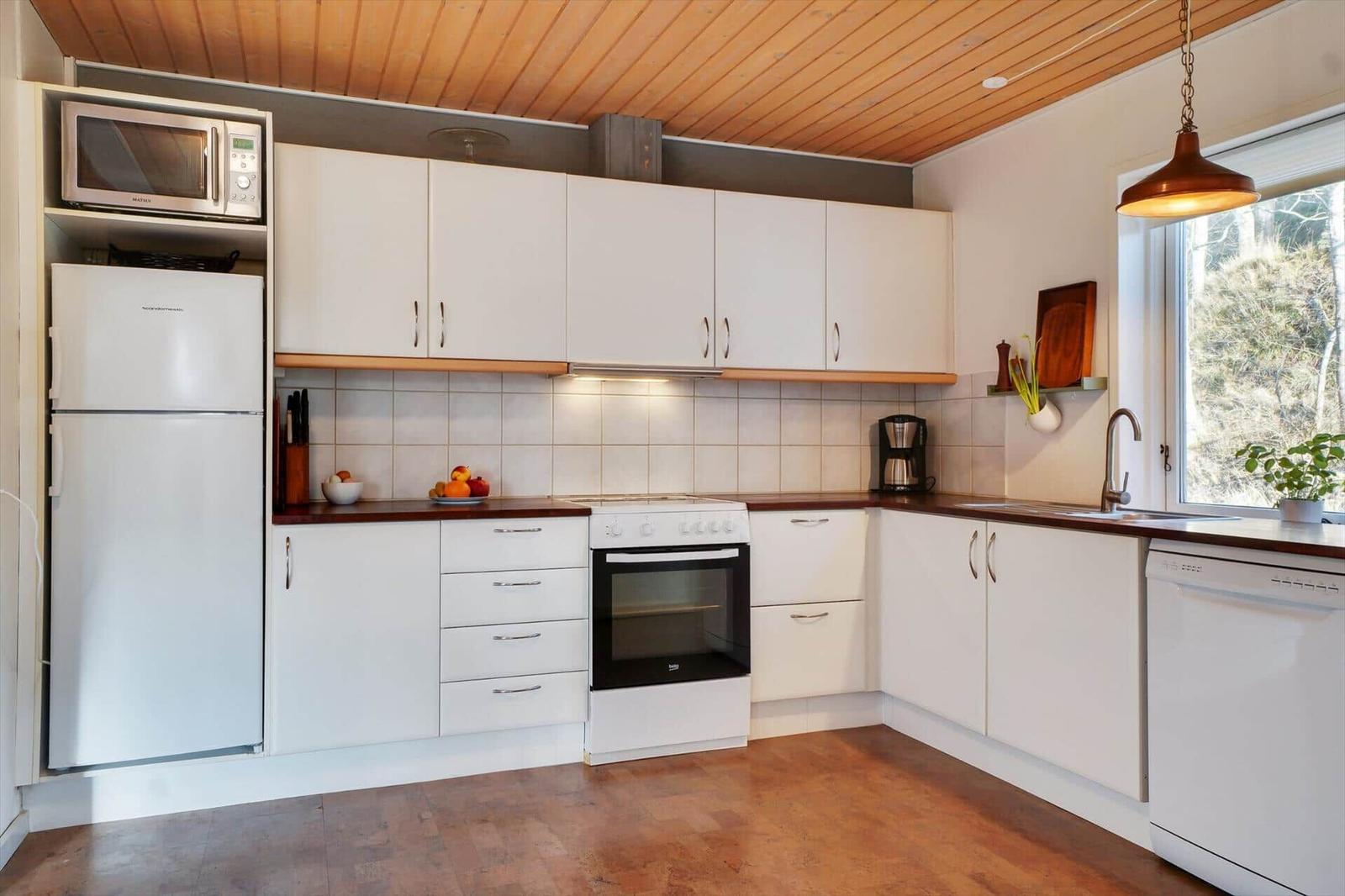 Kitchen with white cabinets, wooden floor, and window view of forest.