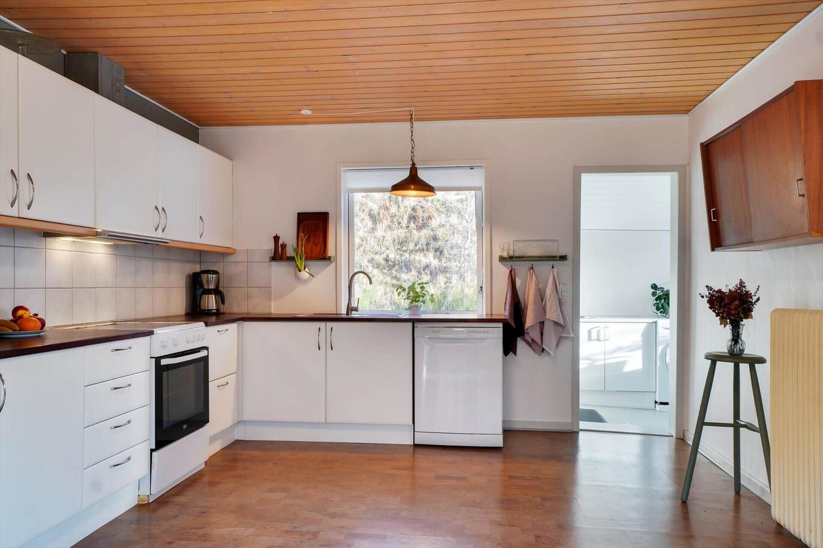 Kitchen with white cabinets, wooden floor, and window to the garden.