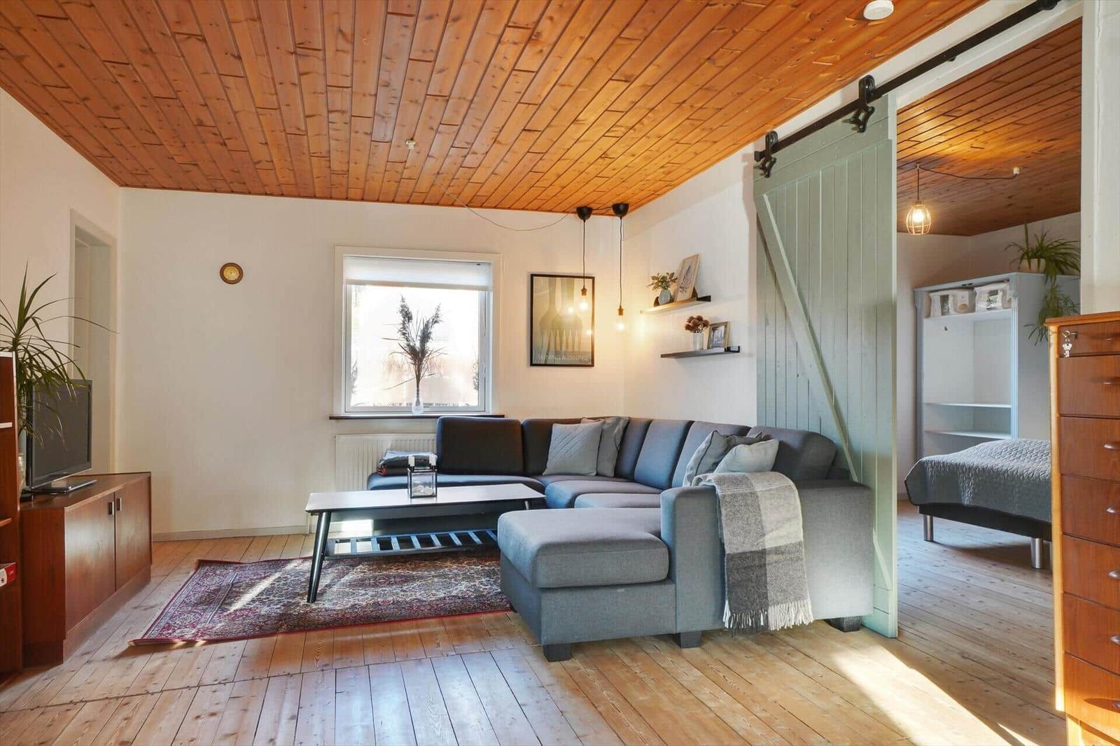 Living room with sofa, coffee table, and wooden floor. Bedroom with bed visible.