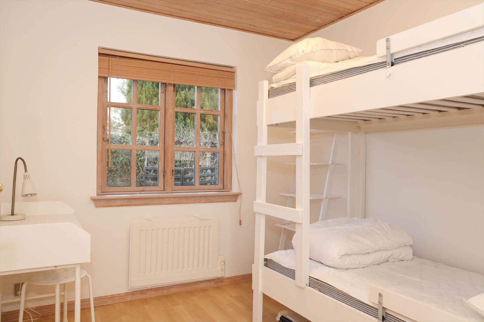 Room with bunk bed, desk, and window with wooden frame.