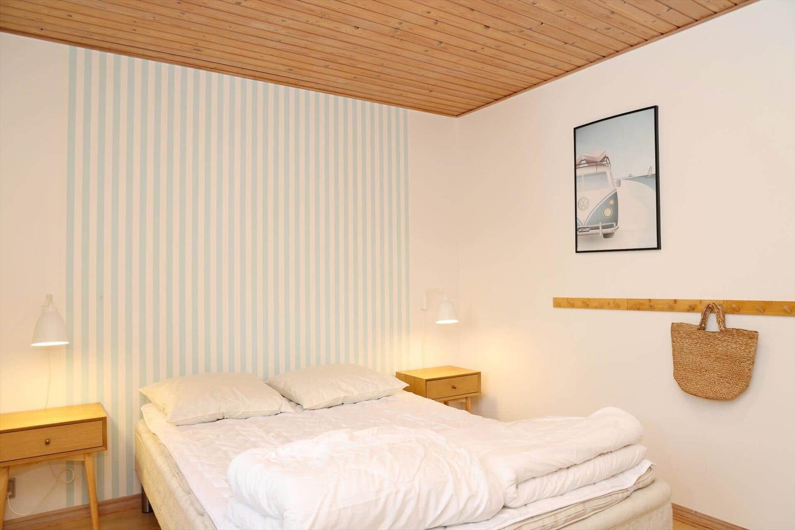Bedroom with bed, nightstands, and striped wall. Wall art and straw bag hang on the wall.