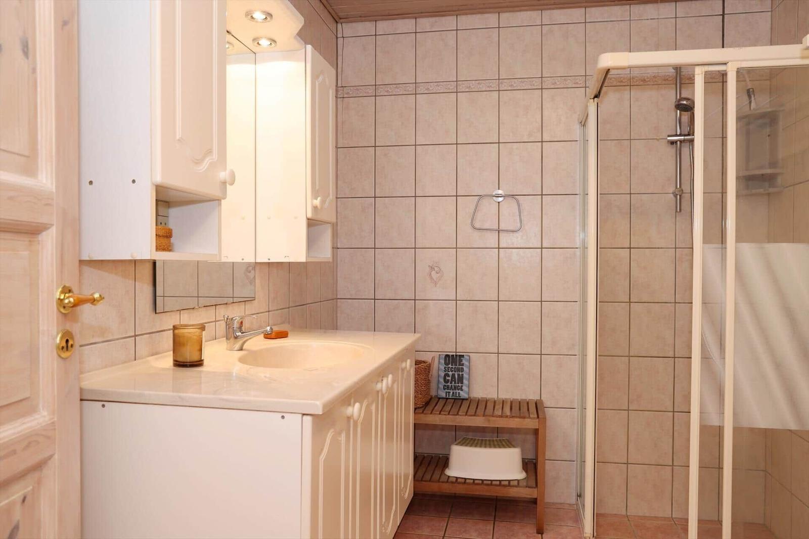 Bathroom with shower, sink, and mirror cabinet. Wooden stool and shower curtain visible.