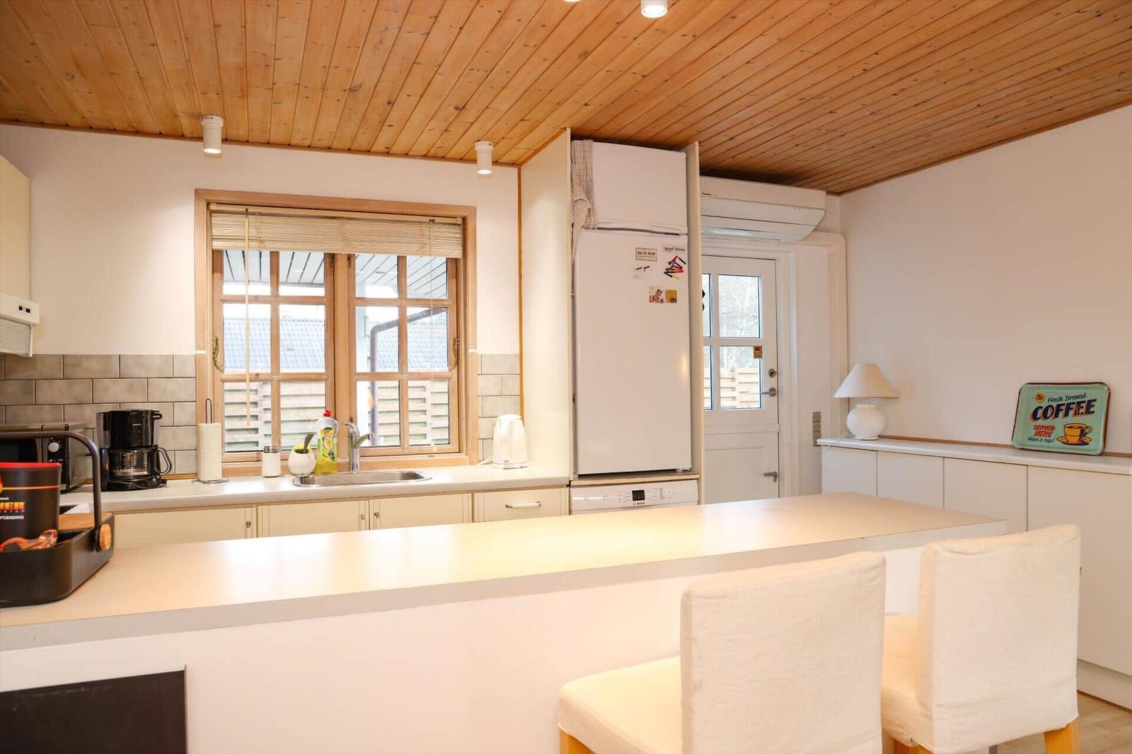 Kitchen with wooden ceiling, refrigerator, sink, and seating at the counter.
