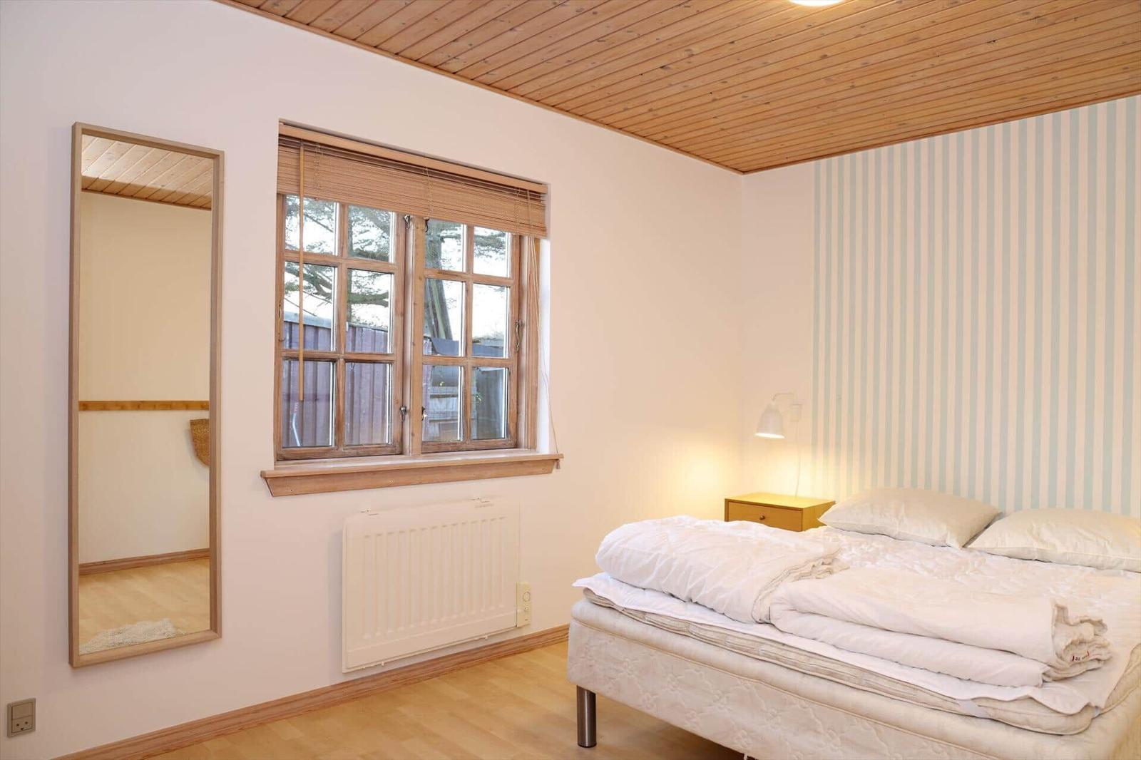 Bedroom with bed, window, mirror, and striped wall.