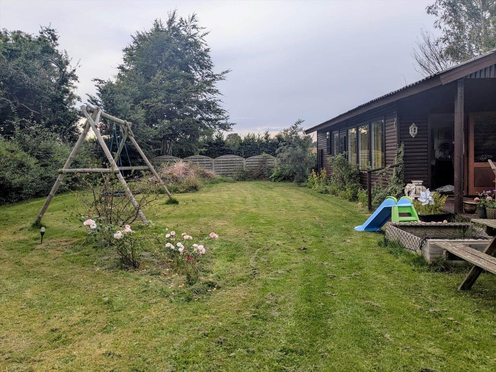 Hinterhof mit Spielgeräten, Rasen und Blumenbeeten neben einem Holzhaus.