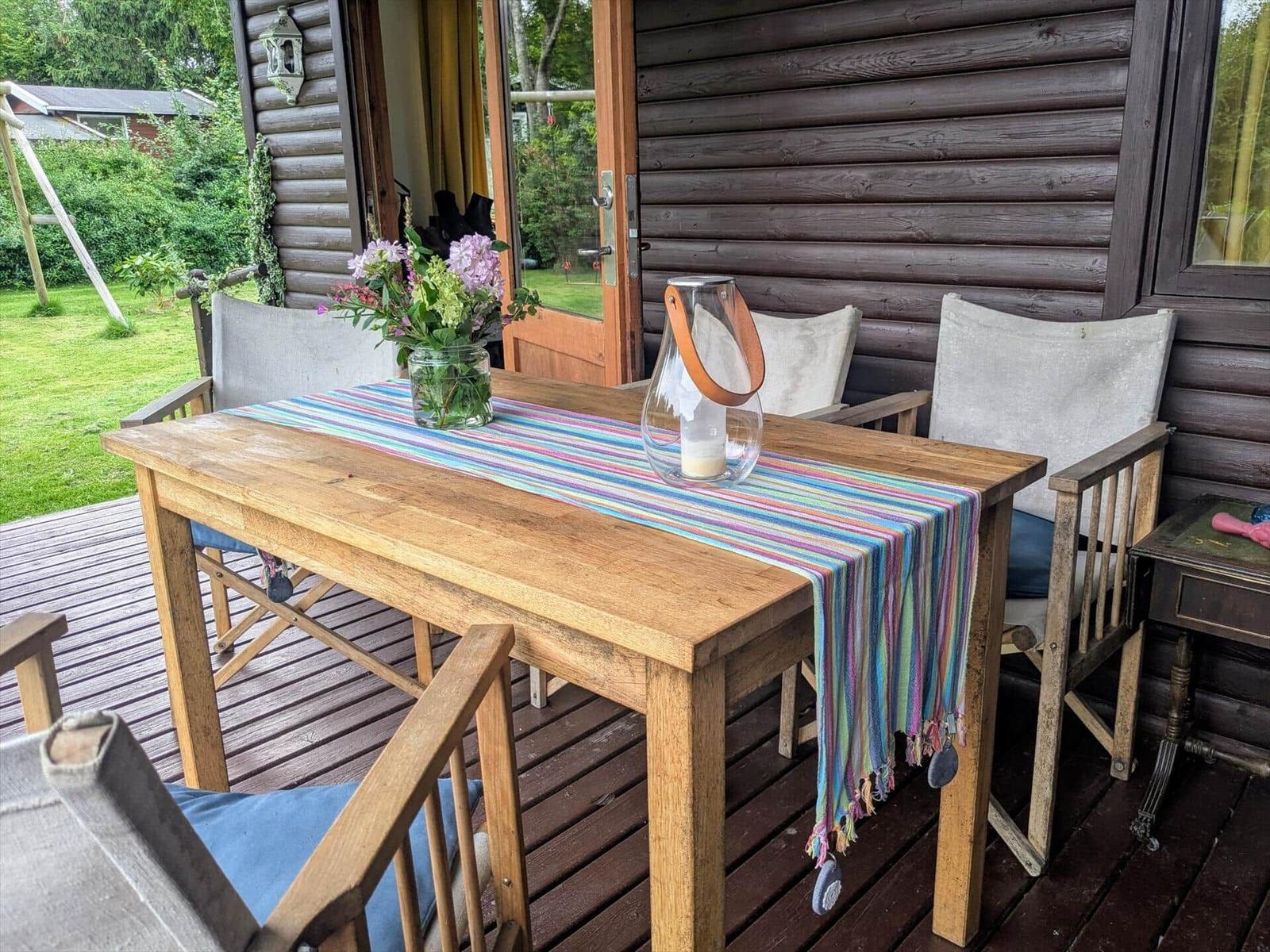 Holztisch mit Stofftischdecke und Blumen auf Terrasse vor Holzhaus