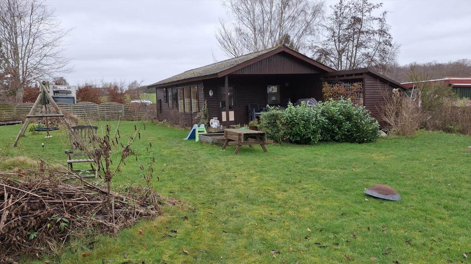 Holzhaus mit Garten, Picknicktisch und Kinderspielplatz.