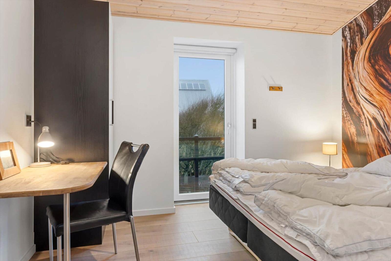 Bedroom with bed, desk, and balcony door. Wooden ceiling and wall art visible.