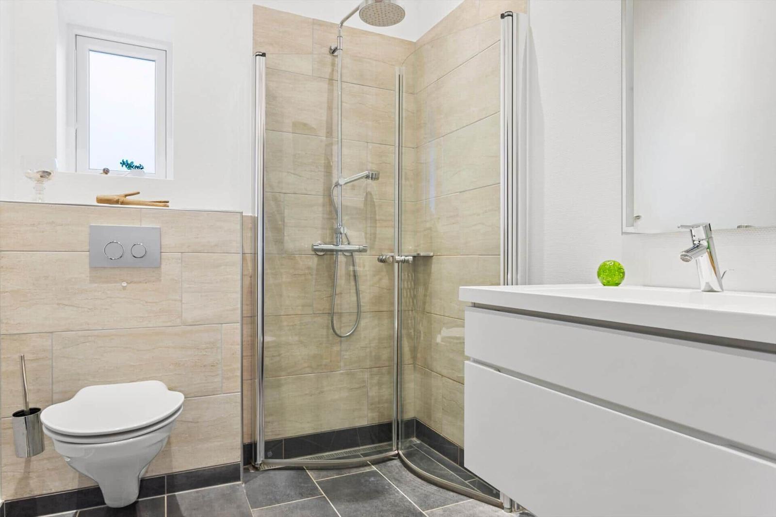 Bath with shower, sink and toilet. Tiled wall and window visible.