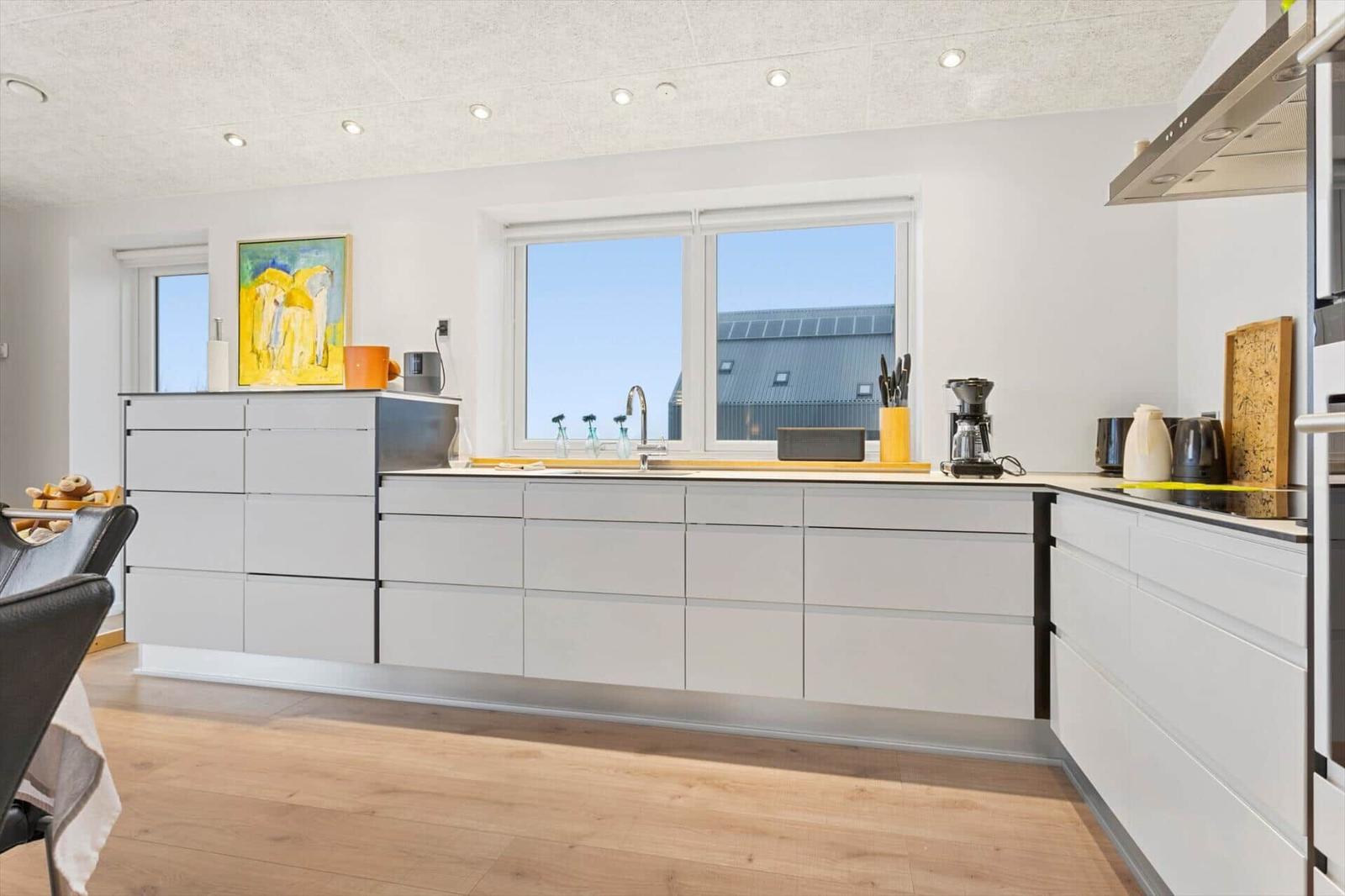 Modern kitchen with white cabinets, wooden floor, and window with view of roof.