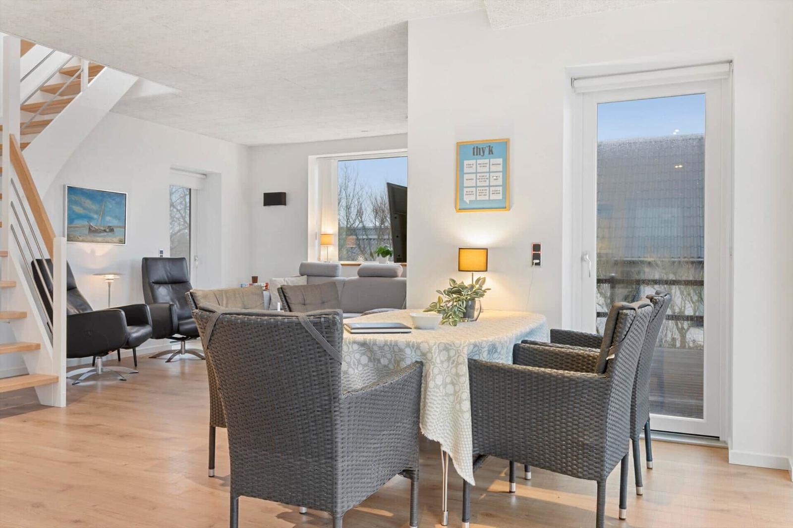 Dining area with table and chairs, living space with sofa and staircase in background.