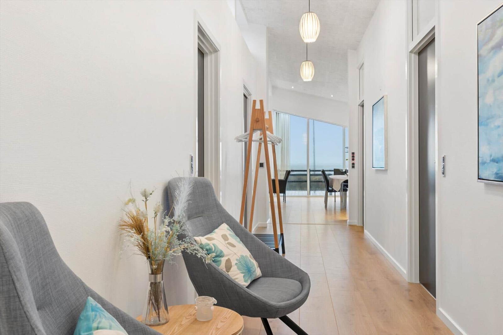 Hallway with gray chairs, wooden floor, and view into dining area with sea view.