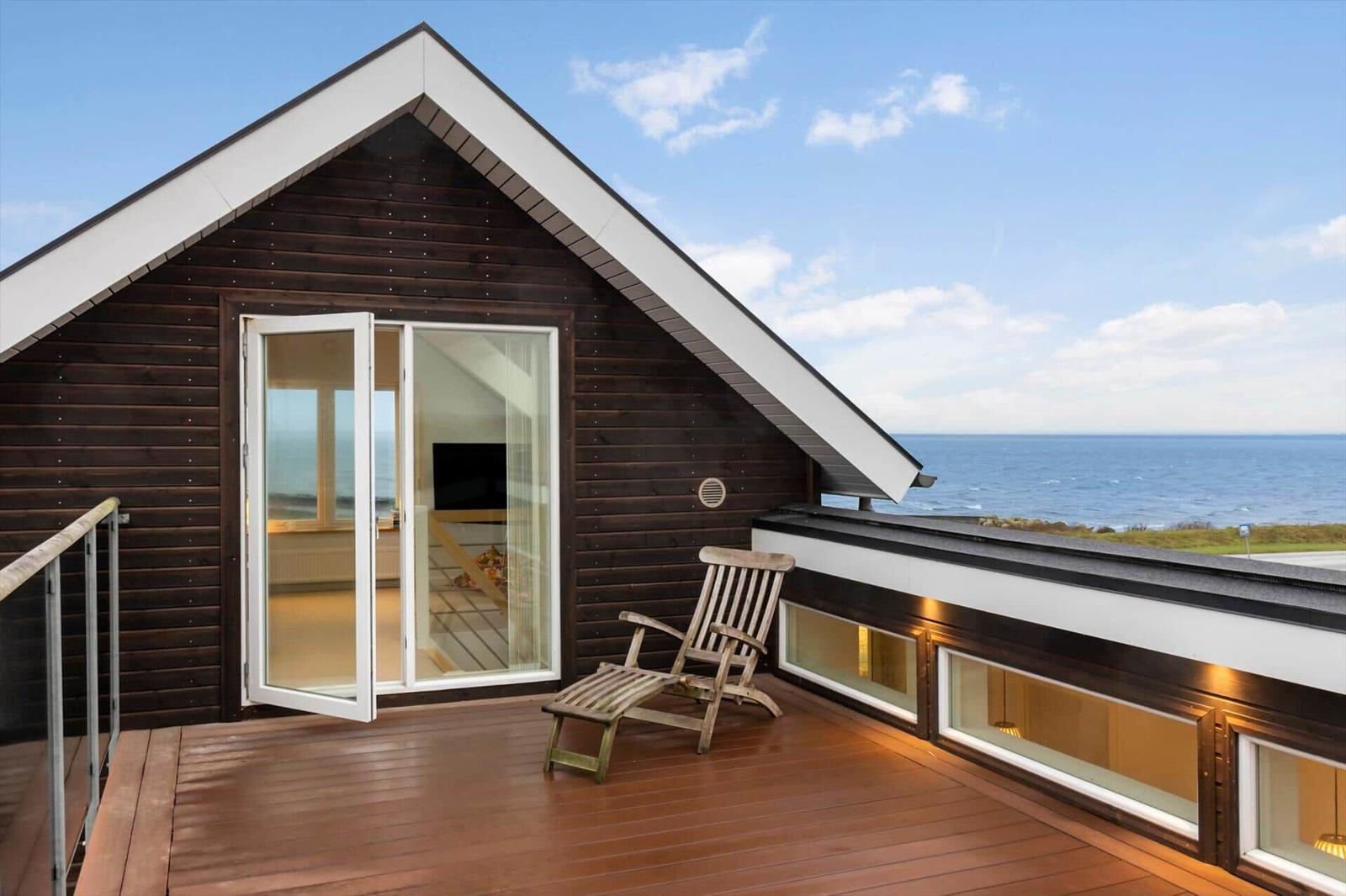 Deck with wooden lounger and ocean view. Glass doors lead inside.